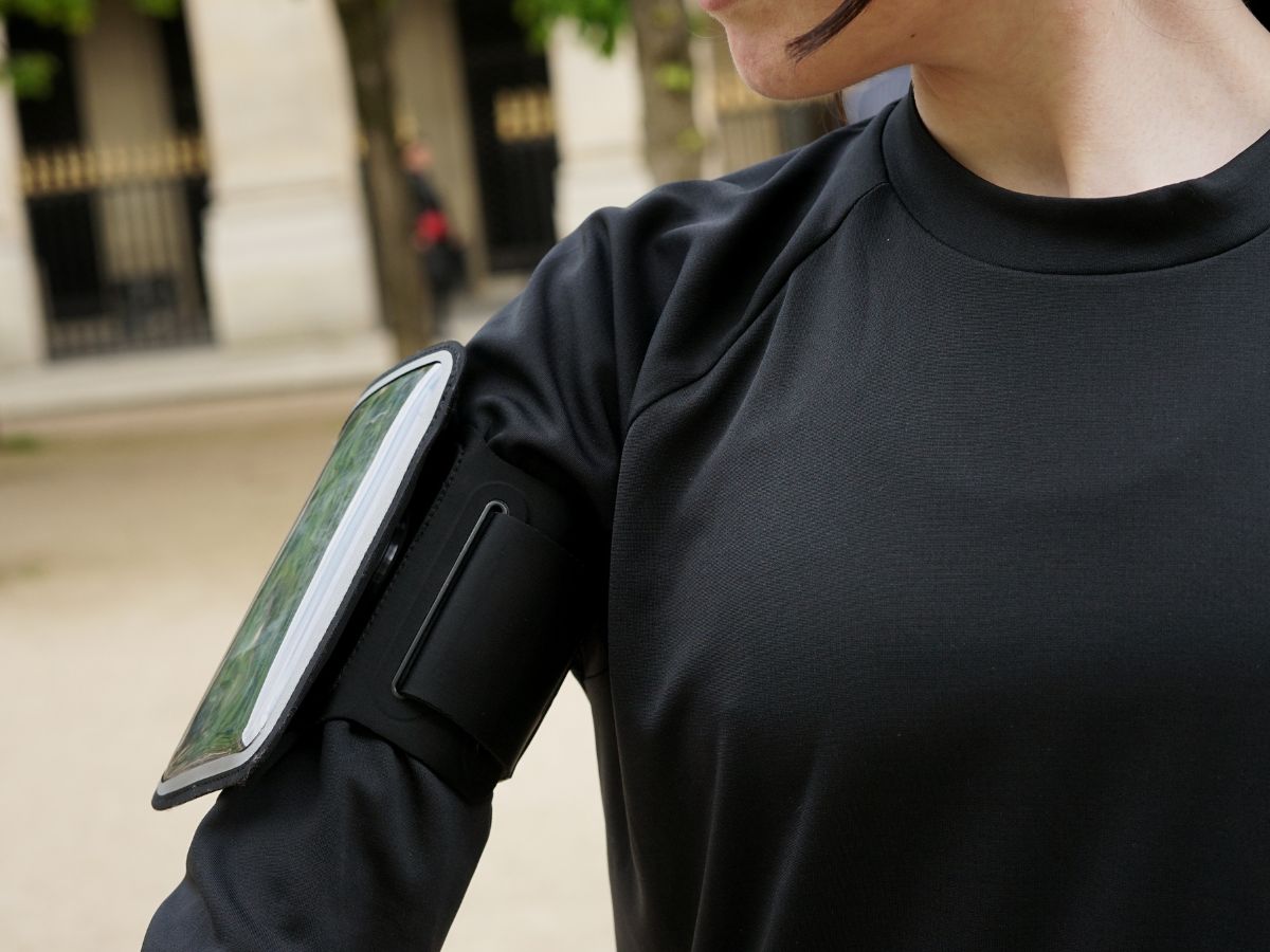 Joggeur en veste imperméable courant sous la pluie avec un brassard étanche visible sur le bras, illustrant la protection des objets électroniques en course.