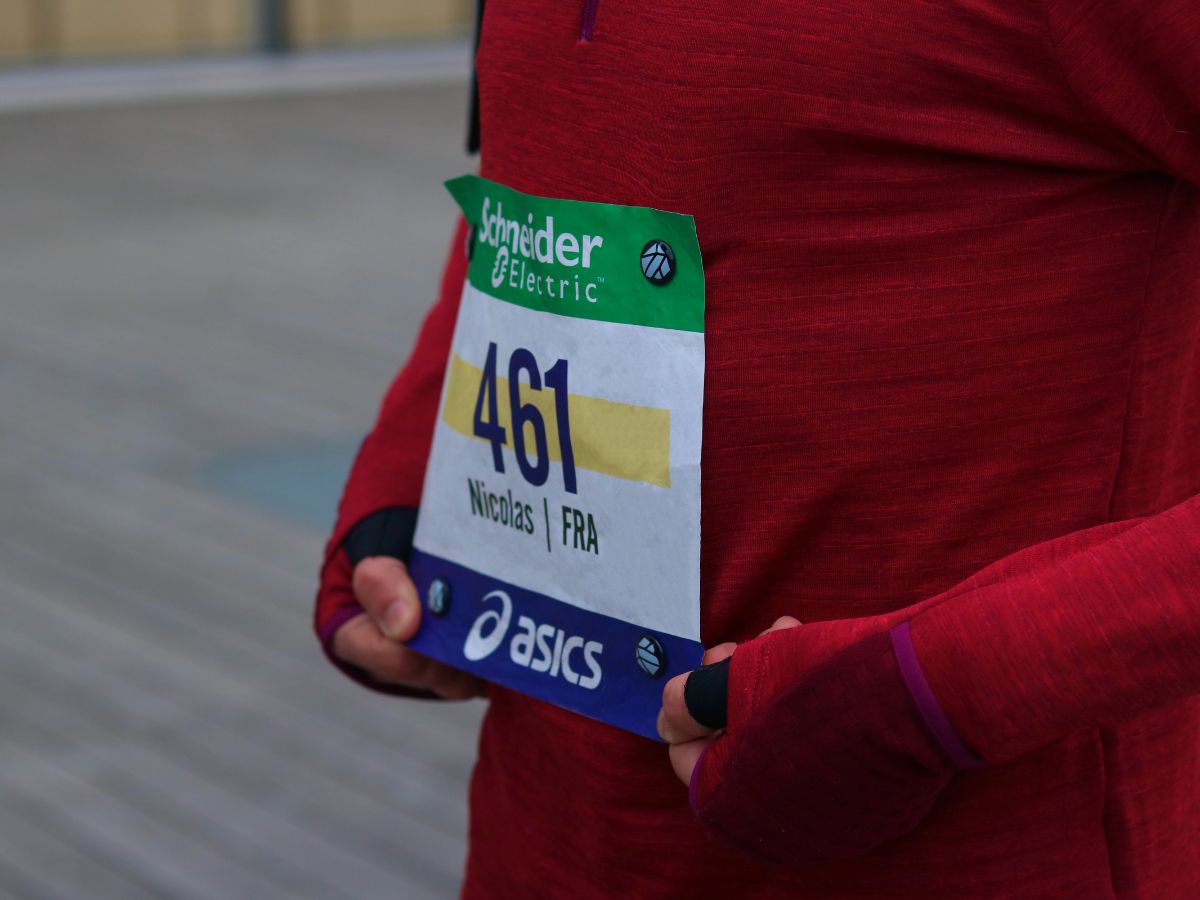 Athlète au départ d’une compétition portant un dossard maintenu par des aimants sur un t-shirt technique, illustrant la préparation optimale pour une course officielle.