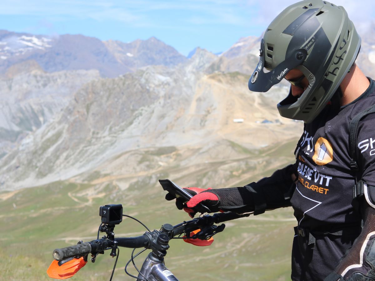 Gros plan sur un support vélo Shapeheart fixé au guidon d’un VTT, smartphone visible, même sur terrain accidenté.