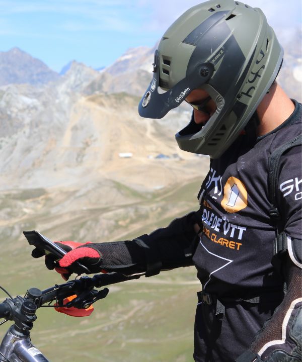 Gros plan sur un support vélo Shapeheart fixé au guidon d’un VTT, smartphone visible, même sur terrain accidenté.